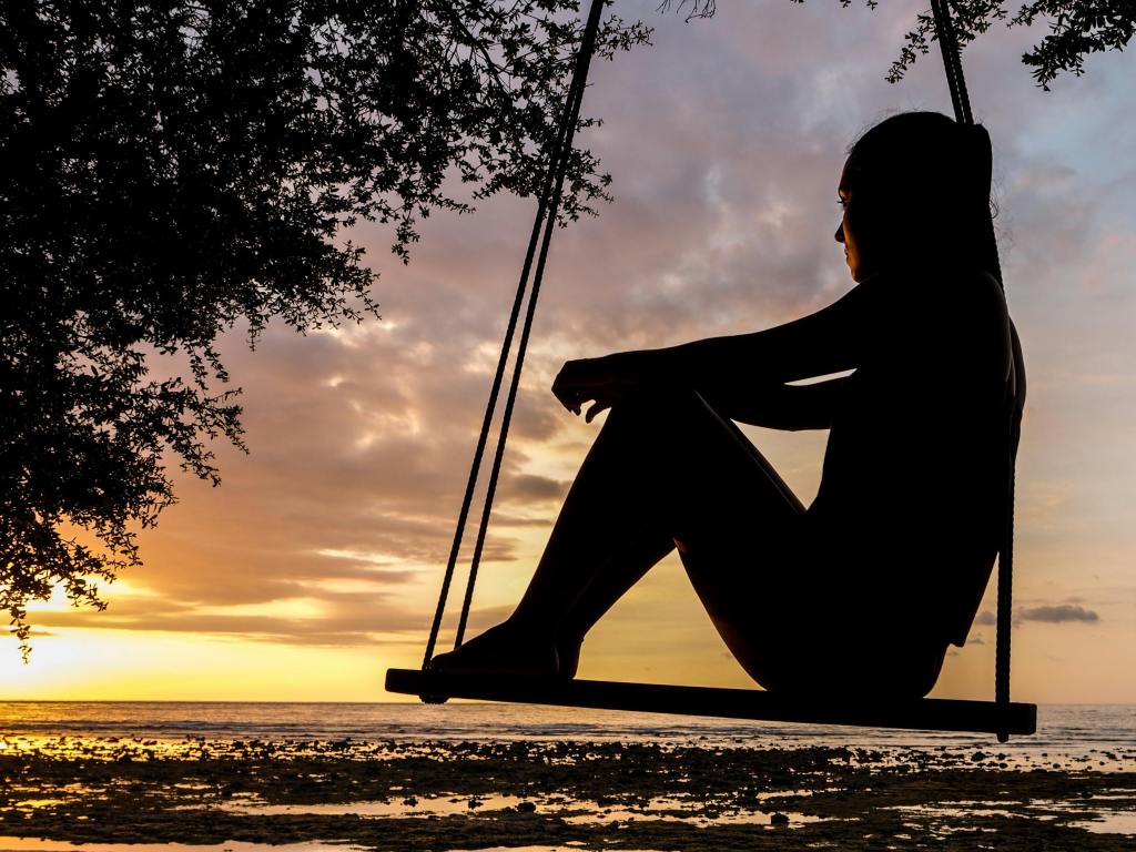 A women sitting on a swing looking at a sunset, deep in thought